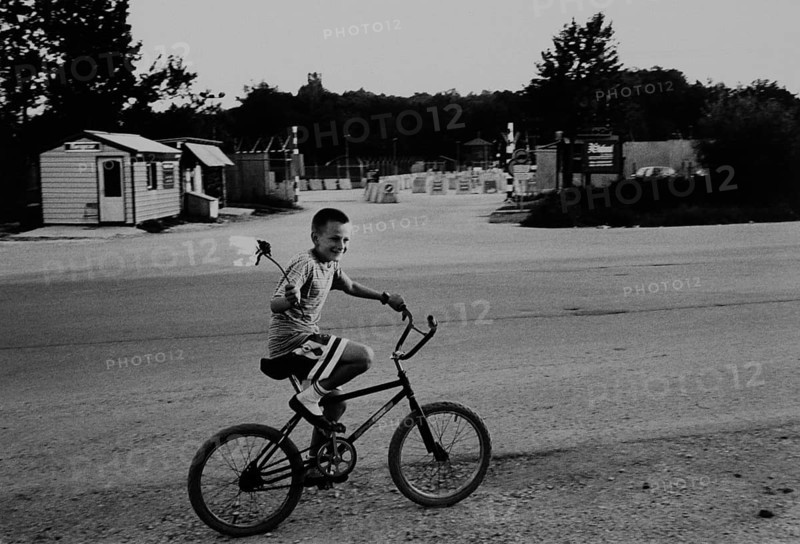 BIH, Bosnia, Tuzla, 17.07.2005, boy with burning stick riding a bicycle in front of the entrance to the airport