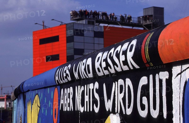 Berlin, DEU, 18.10.1998 -- Site at Potsdamer Platz. Listed remnant of the Berlin Wall painted by artists: Everything is getting better but nothing is going to be good! In the background, visitors on the infobox viewing platform. (art, culture, architecture, tourism)