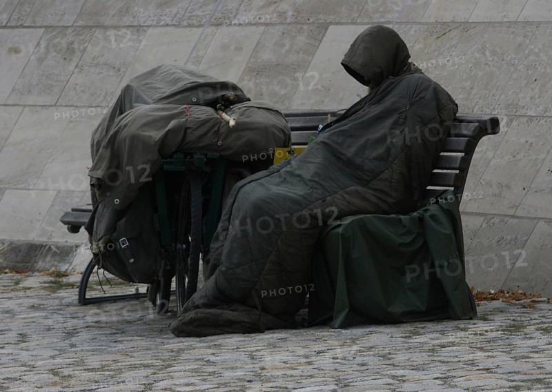 DEU Germany Germany Berlin A homeless person sits on the banks of the Spree opposite the Federal Chancellery, wrapped in his sleeping bag, his bicycle covered