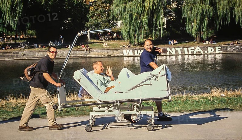 DEU Germany Germany Berlin Two men drive their friend on a hospital bed along the Landwehr Canal near the Urban Hospital on a sunny summer day