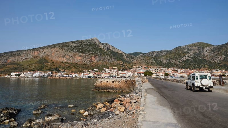 An off-road vehicle on a coastal road with a view of a city and mountains, Monemvasia, Monemvassia, Malvasy, Byzantine small town, rocky island, fortress, Laconia, Peloponnese, peninsula, Greece