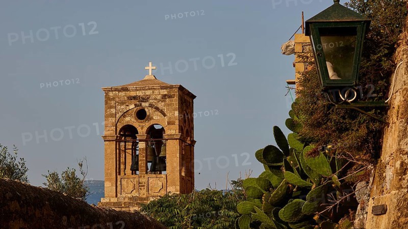 Soft morning light, Holy Church of Christ in Chains, Elkomenos Christos, bell tower with cross next to an old stone wall under a blue sky, surrounded by greenery, Monemvassia, Malvasy, small Byzantine town, rocky island, fortress, Laconia, Peloponnese, peninsula, Greece