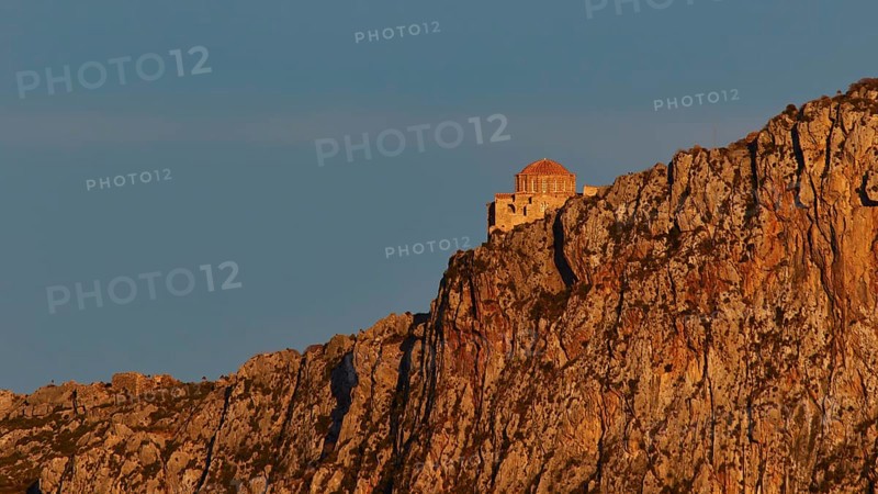 Orhodox church of Hagia Sophia, chapel high on a rock, illuminated in orange evening light, Monemvassia, Malvasy, Byzantine small town, rocky island, fortress, Laconia, Peloponnese, peninsula, Greece