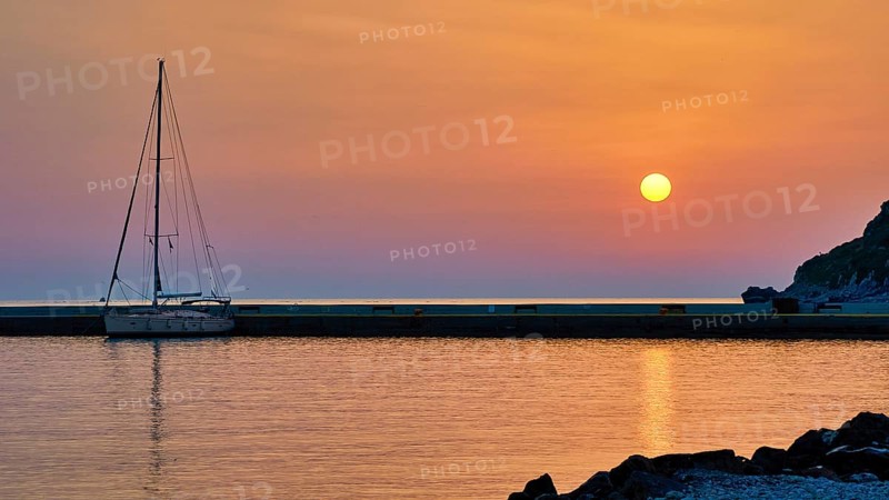 Sailing boat against orange sky and calm sea at sunrise, Monemvasia, Monemvassia, Malvasy, Byzantine small town, rocky island, fortress, Laconia, Peloponnese, peninsula, Greece