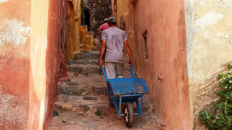A man pulls a wheelbarrow up a narrow, colorful alley, Monemvassia, Malvasy, small Byzantine town, rocky island, fortress, Laconia, Peloponnese, peninsula, Greece