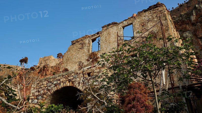 Dilapidated stone structure nestled in lush vegetation under clear skies, Monemvasia, Monemvassia, Malvasy, Byzantine small town, rocky island, fortress, Laconia, Peloponnese, peninsula, Greece