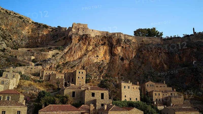 Drone shot, medieval buildings on a rocky cliff overlooking the Mediterranean Sea at sunset, Monemvasia, Monemvassia, Malvasy, Byzantine small town, rocky island, fortress, Laconia, Peloponnese, peninsula, Greece
