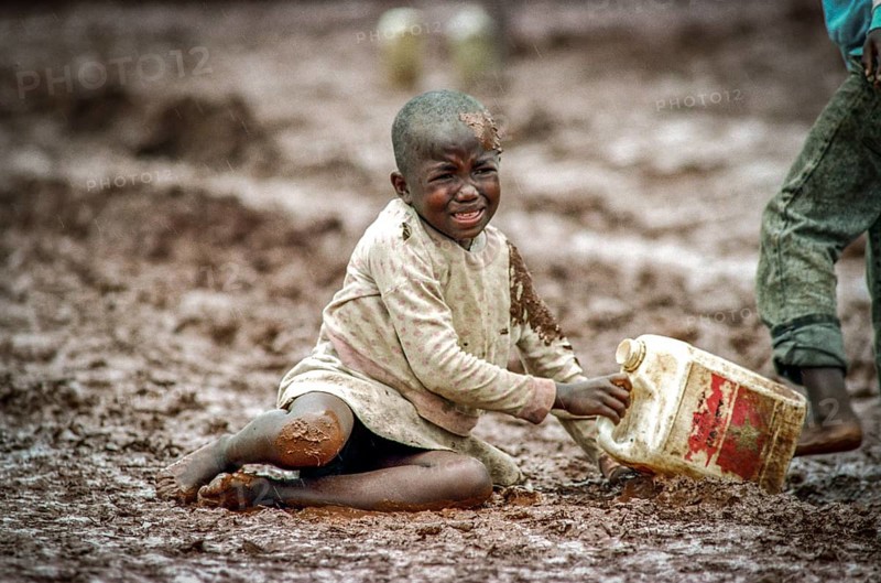 TZA Tanzania scene in the Benaco Camp refugee camp, to which up to 500, 000 Rwandan Tutsis fled the genocide in their country. A refugee child has gone off on a muddy path. TZA Tanzania Scene at the Benaco Camp, where an estimate of 500, 000 Rwandan Tutsi refugees fled the genocide in their country. A Refugee Kid, Send for Water Supply, Sliped on a Muddy Path