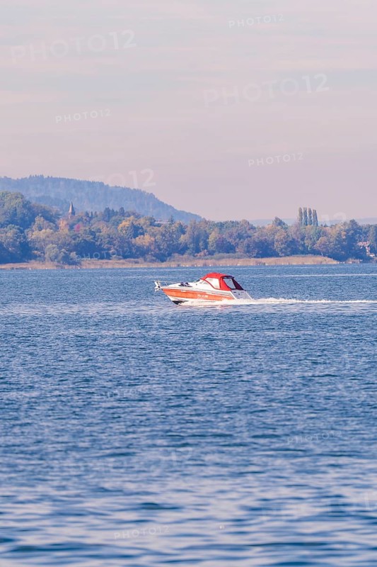 A motorboat sails at high speed across a quiet lake in autumn surroundings, boat trip, Lake Constance, Germany