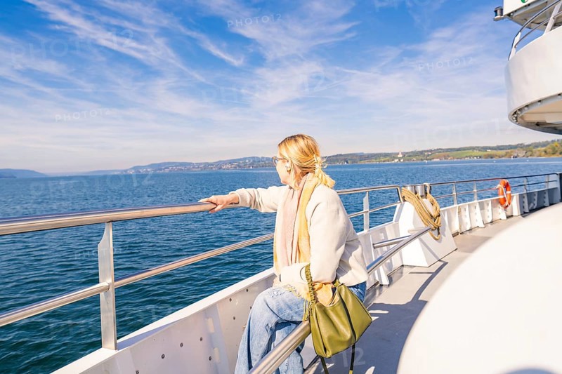 A woman stands relaxed at the railing of a ship and looks out to sea in sunny weather, Schiff Fahrt, Lake Constance, Germany