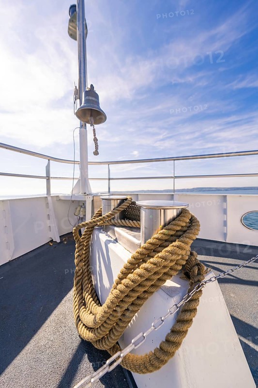 A ship deck with thick ropes and a bell, in front of a clear blue sky at sea, boat trip, Lake Constance, Germany