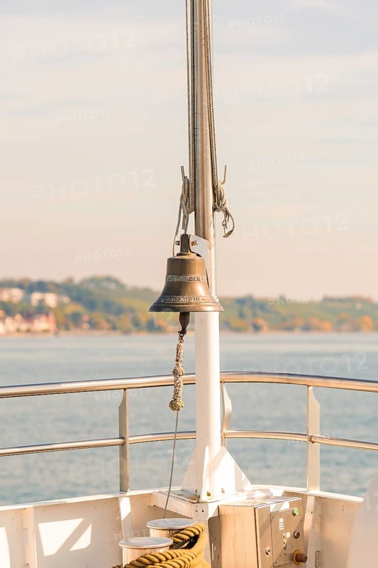 Bell on a ship deck with a view of a sunny coastal landscape, boat trip, Lake Constance, Germany