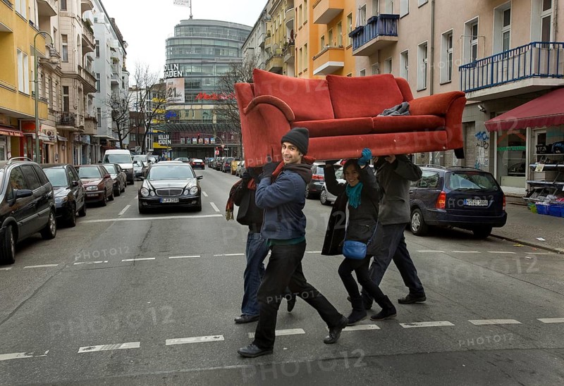 DEU Berlin Young people carry a sofa across Fuldastraße in Berlin Neukölln. The former problem district has been changing for some time due to the influx of students and young creative people from home and abroad. Germany Berlin A Group of New Berlin Citizens Carry a Red Sofa Across the Street