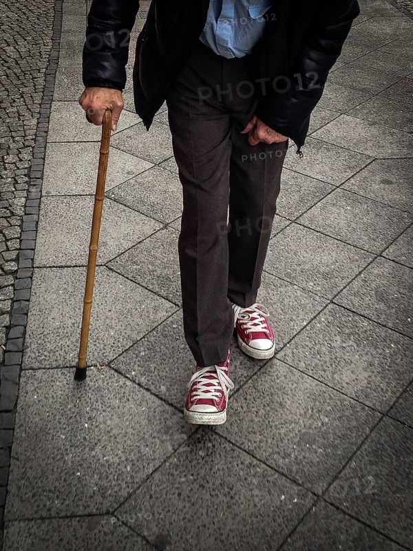 DEU Germany Germany Berlin Old man with a crutch walking through the German capital wearing Converse shoes