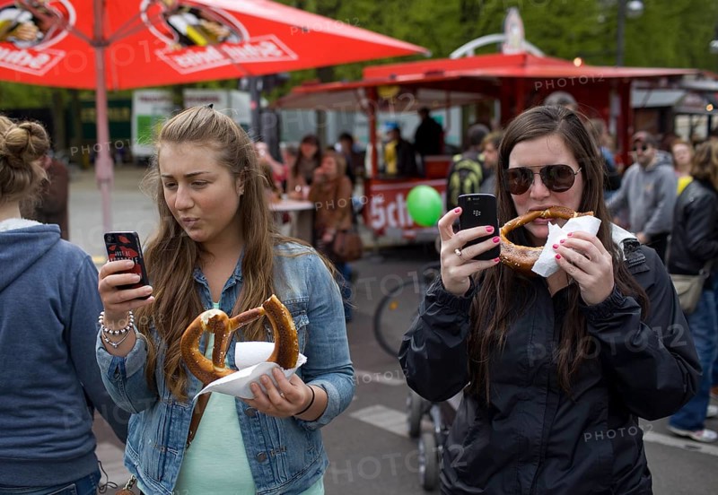 GERMANY Young woman are filming a rally with their mobile phones while eating pretzels. Germany Berlin Young woman shooting with their mobile phones as they are eating pretzels during the May Day protest