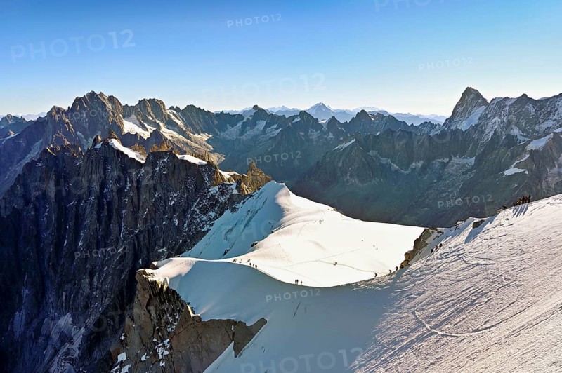 Mountaineers climb over a snow-covered ridge, behind Aiguille Verte, Les Droites, Les Courtes, Grandes Jorasses, Aiguille du Midi mountain station, Chamonix-Mont-Blanc, Haute-Savoie, France