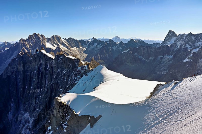Mountaineers climb over a snow-covered ridge, behind Aiguille Verte, Les Droites, Les Courtes, Grandes Jorasses, Aiguille du Midi mountain station, Chamonix-Mont-Blanc, Haute-Savoie, France