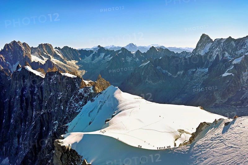 Mountaineers climb over a snow-covered ridge, behind Aiguille Verte, Les Droites, Les Courtes, Grandes Jorasses, Aiguille du Midi mountain station, Chamonix-Mont-Blanc, Haute-Savoie, France