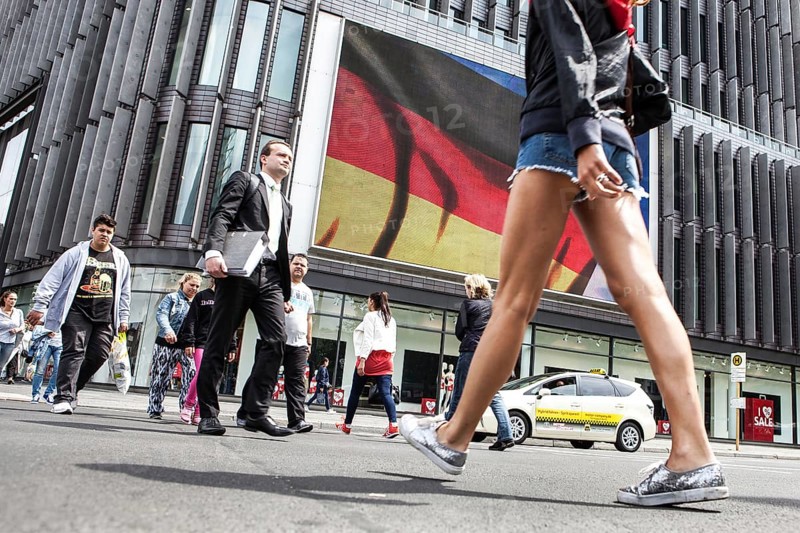 DEU Germany Germany Berlin Passers-by in front of a projection screen on Kurfürstendamm, on which a commercial featuring a large German flag is being broadcast