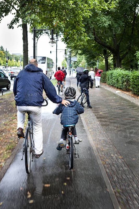 DEU Germany Germany Berlin Cyclists have their arms on a child's back as they cycle towards the Brandenburg Gate