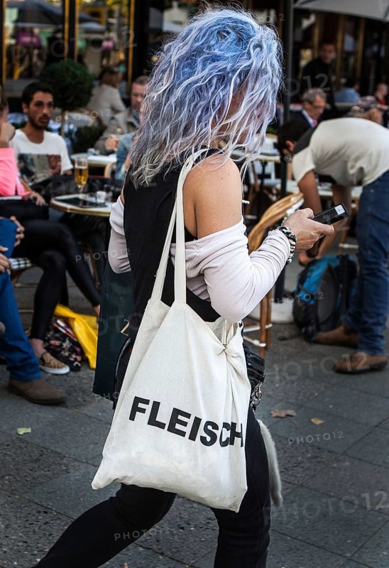 DEU Germany Germany Berlin Woman with blue-dyed hair wears a cloth bag with the inscription Flesh while she is strolling into her smartphone