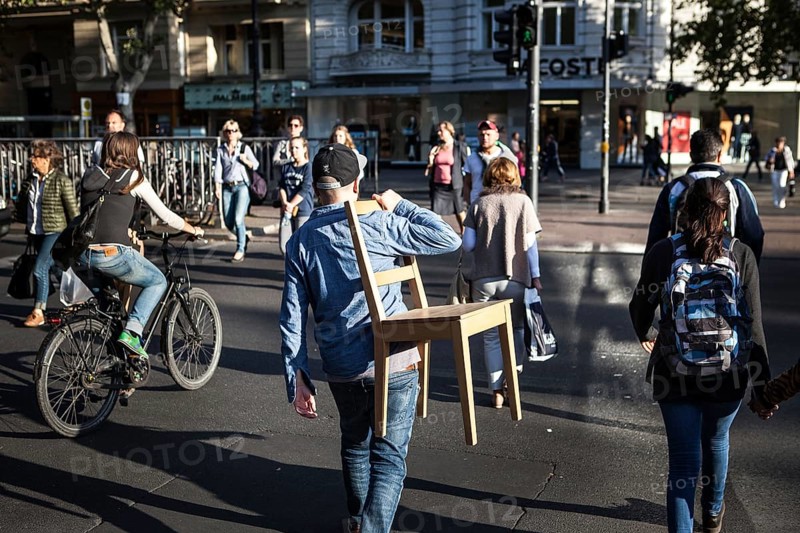 DEU Germany Germany Berlin Man with a chair over his shoulder crosses a pedestrian traffic light on Kudamm