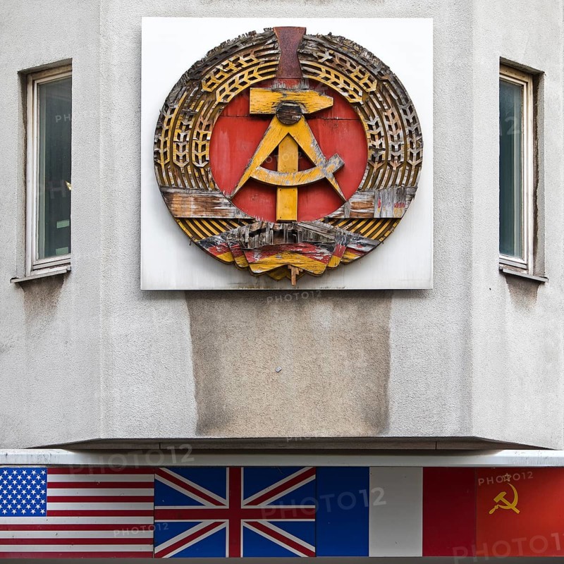 Old building of the Wall Museum — Museum Haus am Checkpoint Charlie with the old coat of arms of the GDR and the flags of the occupying powers, Berlin, Germany
