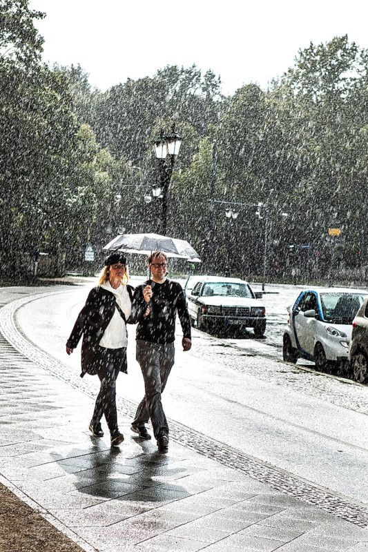 DEU Germany Germany Berlin A couple walking with an umbrella through a summer rain shower at the Victory Column
