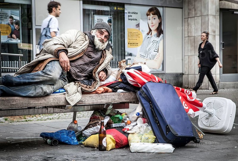 DEU Germany Germany Berlin A homeless person sits on a bench next to his belongings in a square in Schöneberg