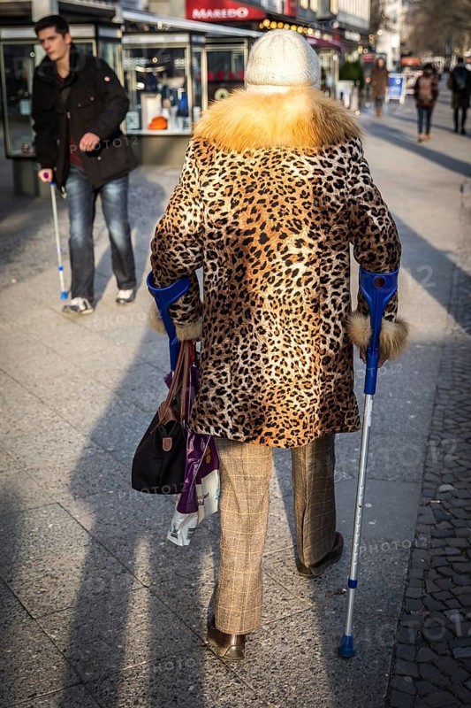 DEU Germany Germany Berlin A woman wears a leopard cloak while using crutches on the Kudamm to pass a man with a crutch