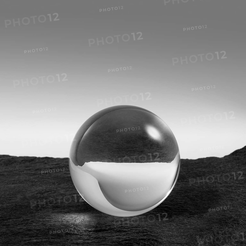 A clear crystal ball on rough dark grey stone surface in front of red back