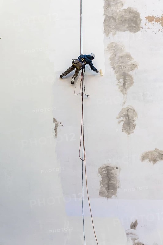 DEU Germany Germany Berlin A worker painting a façade while hanging from a rope