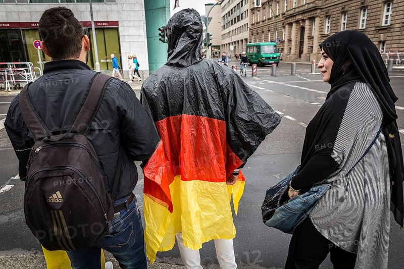DEU Germany Germany Berlin Two tourists with rain capes in the colours of Germany are accompanied by Muslim friends