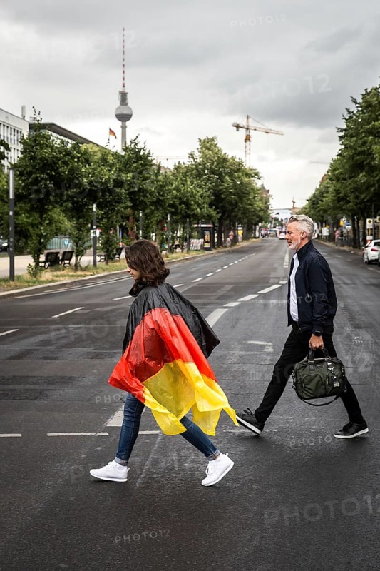 DEU Germany Germany Berlin Tourist with rain capes in the colours of Germany crosses a pedestrian crossing on the street Unter den Linden