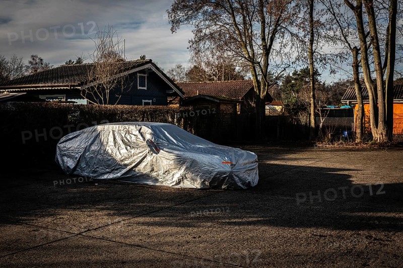 DEU Germany Germany Berlin A car, wrapped in a tarpaulin, is parked in a car park next to an allotment garden in the Grunewald forest