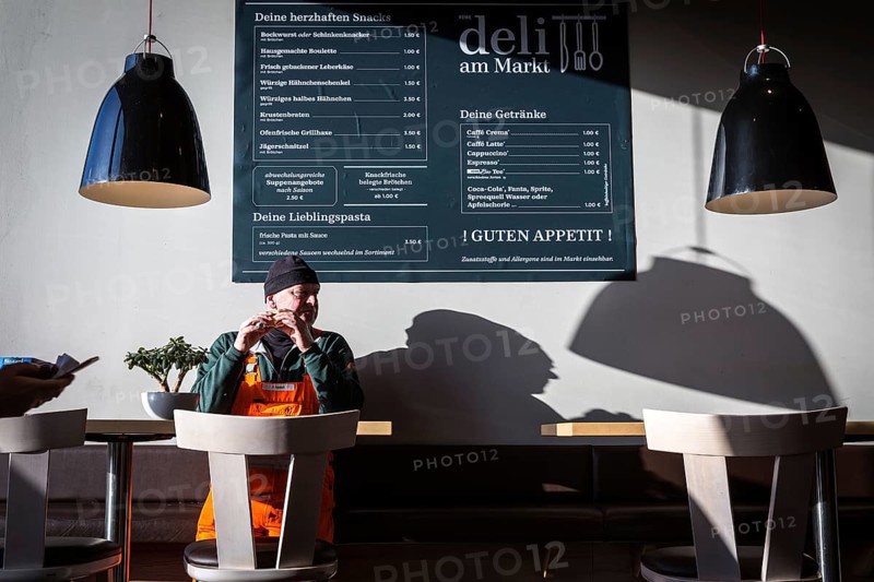 DEU Germany Germany Berlin A man eats a sandwich in a snack bar attached to the Rewe supermarket in Teltow