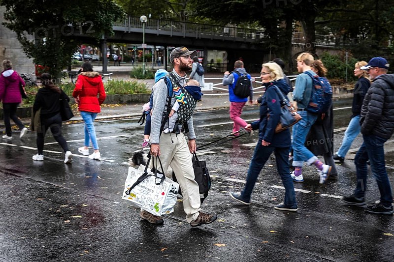 DEU Germany Germany Berlin A father with his two children on his stomach and back walks with shopping bags along the street at Nollendorfplatz