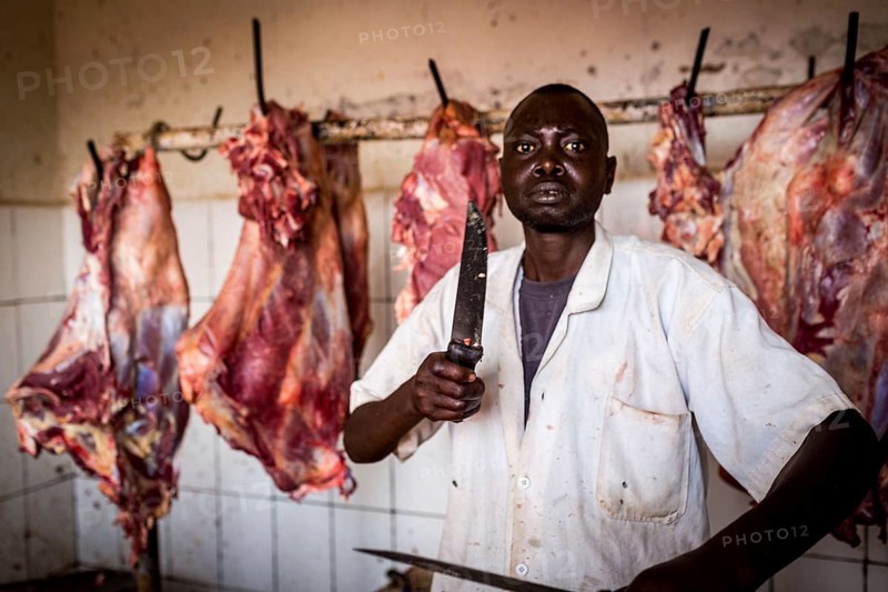 RWA RWANDA Rwanda Kayonza A butcher sharpens his knives in front of pieces of meat. He poses for the photographer ___