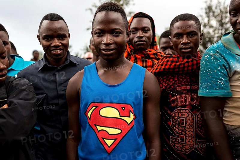 TZA TANZANIA Benaco Young people listen to a nappy salesman in a marketplace. A man in a superman shirt
