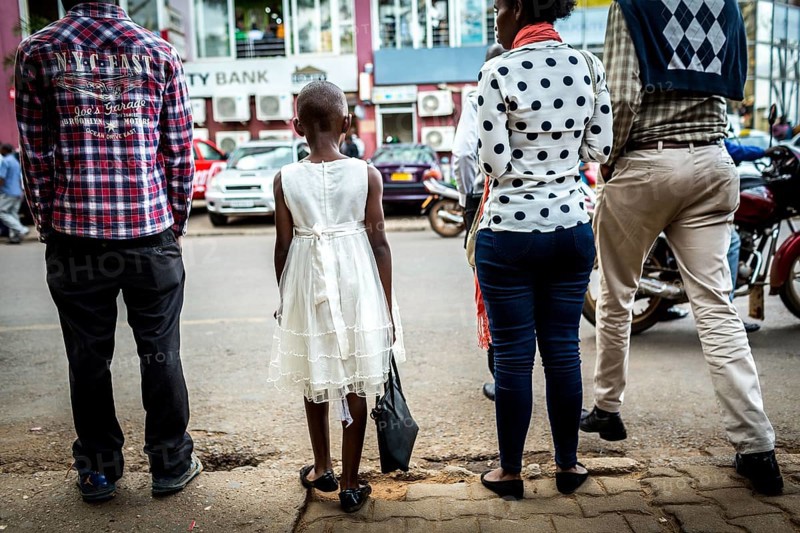 RWA RWANDA RUANDA Kigali A young girl with a white dress and handbag waits with others until she can cross the road