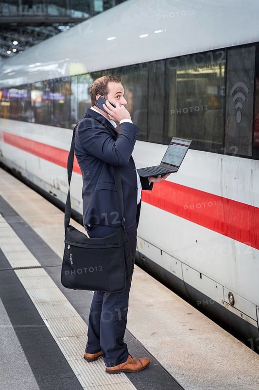 DEU Germany Germany Berlin A passenger stands in front of an ICE train at Berlin Central Station with a laptop on his phone