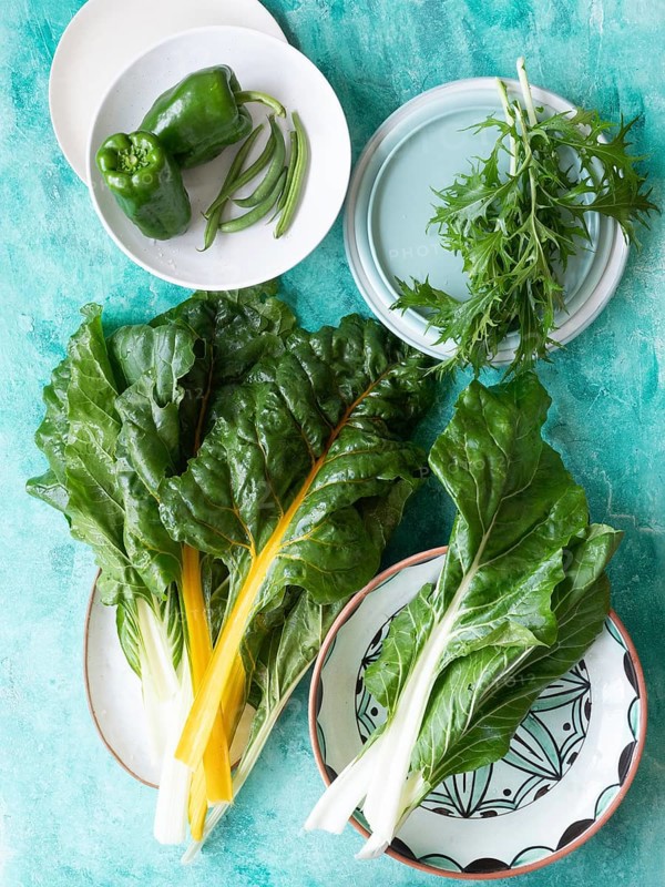 Fresh green chard, bell pepper, green beans, and mizuna on plates