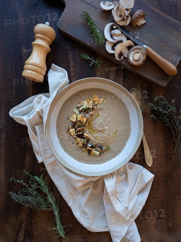 Mushroom soup with rosemary, thyme, garlic croutons, and raw mushrooms on a dark wood background