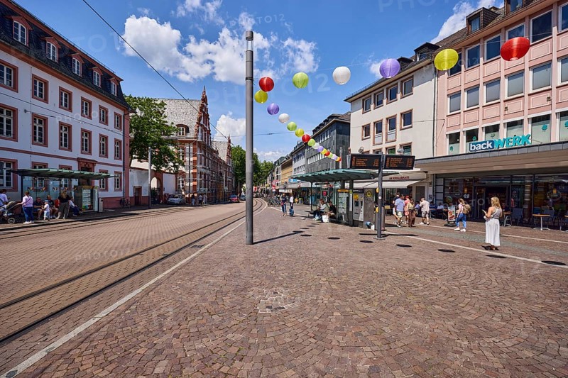 Schillerplatz tram stop, bakery backwerk, overhead lines, general architecture, houses, residential buildings and commercial buildings, lantern, paving stone walkway, concrete paving street, decoration, lanterns, pedestrians and people waiting for means of transport as a secondary motif, blue sky, cumulus clouds, Schillerstraße, Mainz, state capital, district-free city, Rhineland-Palatinate, Germany