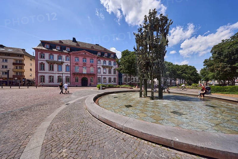 Shrove Tuesday fountain, fountain with bronze sculptures, sculptor Blasius Spreng, architect Helmut Gräf, general architecture, houses, paving stone flooring, pedestrians and seated people as secondary motifs, trees, blue sky, cumulus clouds, Schillerplatz square, Mainz, state capital, district-free city, Rhineland-Palatinate, Germany