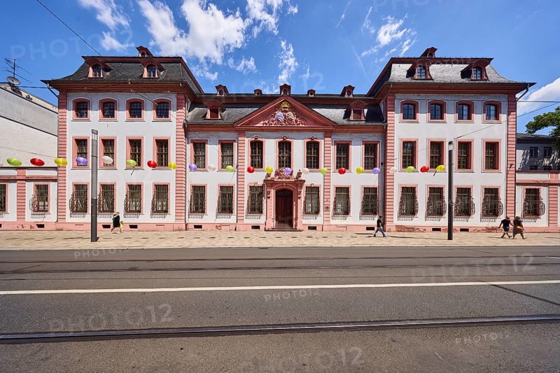 Erthaler Hof, Adelshof, architectural style classicism, façade with windows and door, historic building, lantern, tram tracks, asphalt road, decoration, lanterns, pedestrians as accessories, blue sky, cumulus clouds, Schillerstraße street, Mainz, state capital, district-free city, Rhineland-Palatinate, Germany