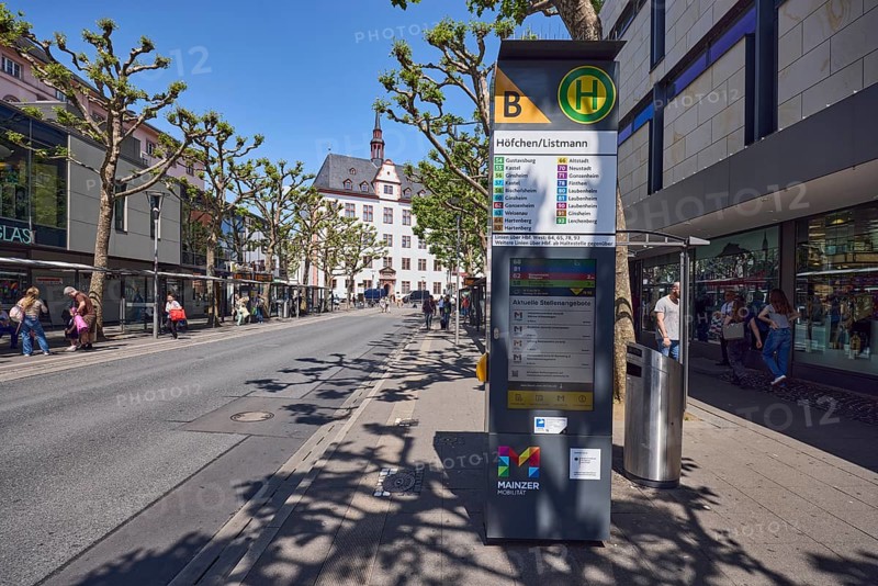 Mainz Höfchen Listmann bus stop, bus platform B, commercial building, general architecture, trees, common plane tree (Platanus ×hispanica), pedestrians as accessories, people waiting for means of transport, blue sky, cloudless, Schöfferstraße, Mainz, state capital, district-free city, Rhineland-Palatinate, Germany