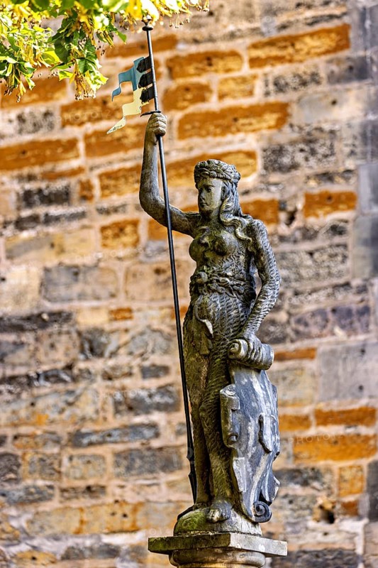 Statue of a figure carrying a flag and a shield in front of an old stone wall, statue and monument in the old town of Arnstadt in Thuringia