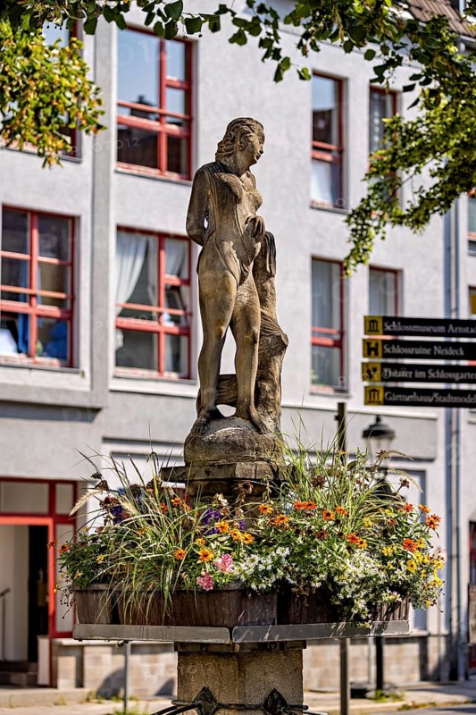 Figure on a fountain with flower frame in front of a building with windows, statue and monument in the old town of Arnstadt in Thuringia