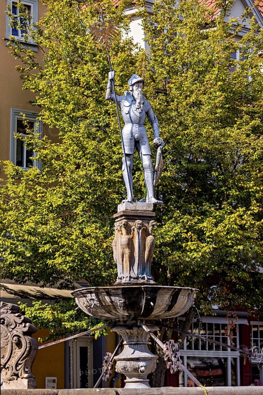 Metal statue of a warrior on a fountain surrounded by green trees, statue and monument in the old town of Arnstadt in Thuringia